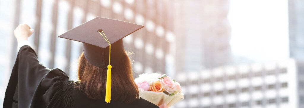 Back side young female student holding flower bouquet on graduation ceremony